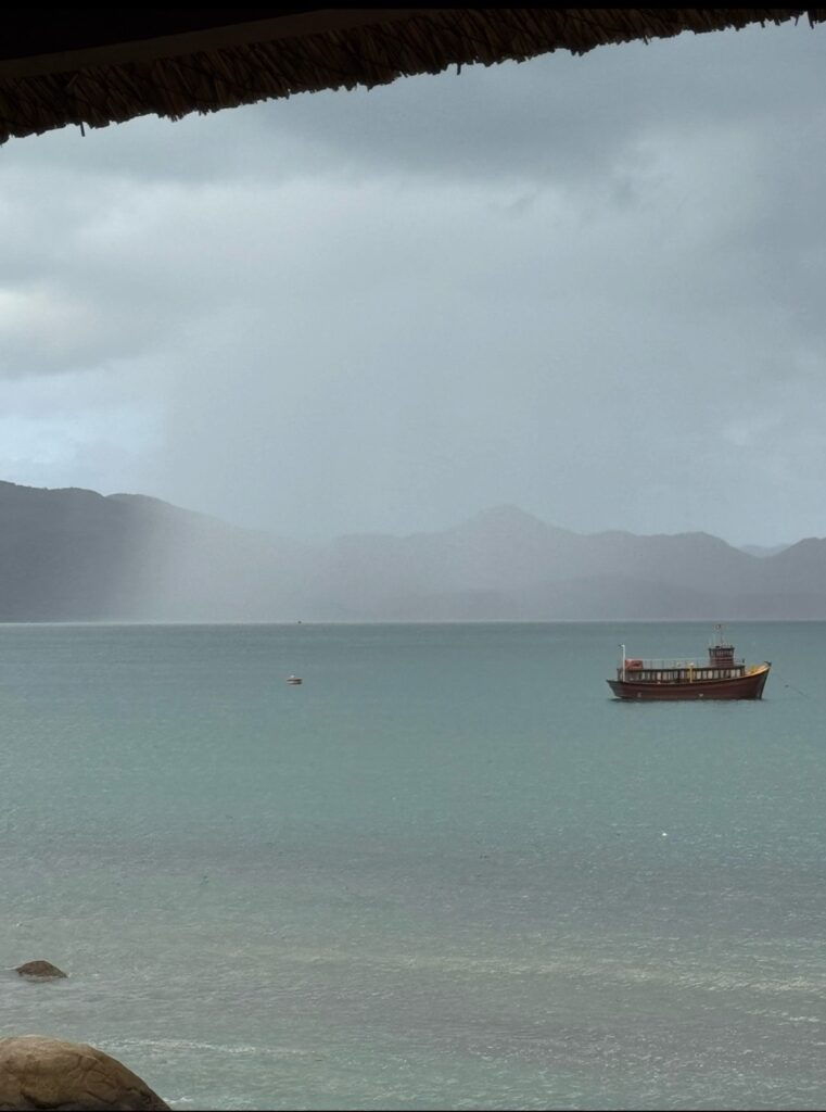 A single boat resting on calm water during rainfall, reflecting stillness and uncertainty.